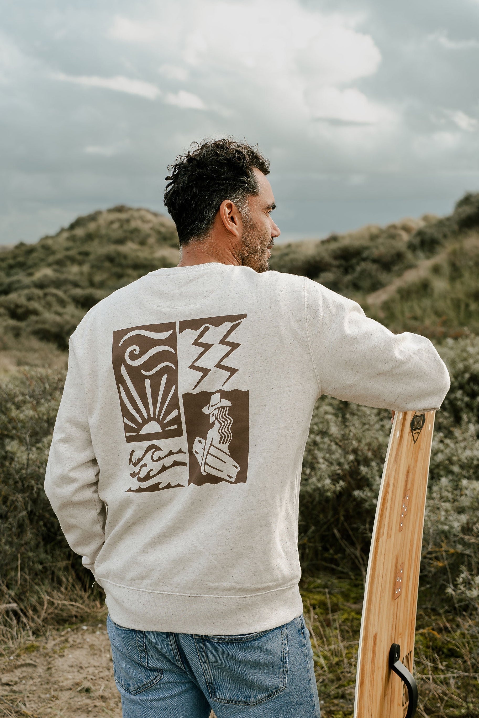 Man wearing a white sweatshirt with a design on the back, standing in a grassy field.